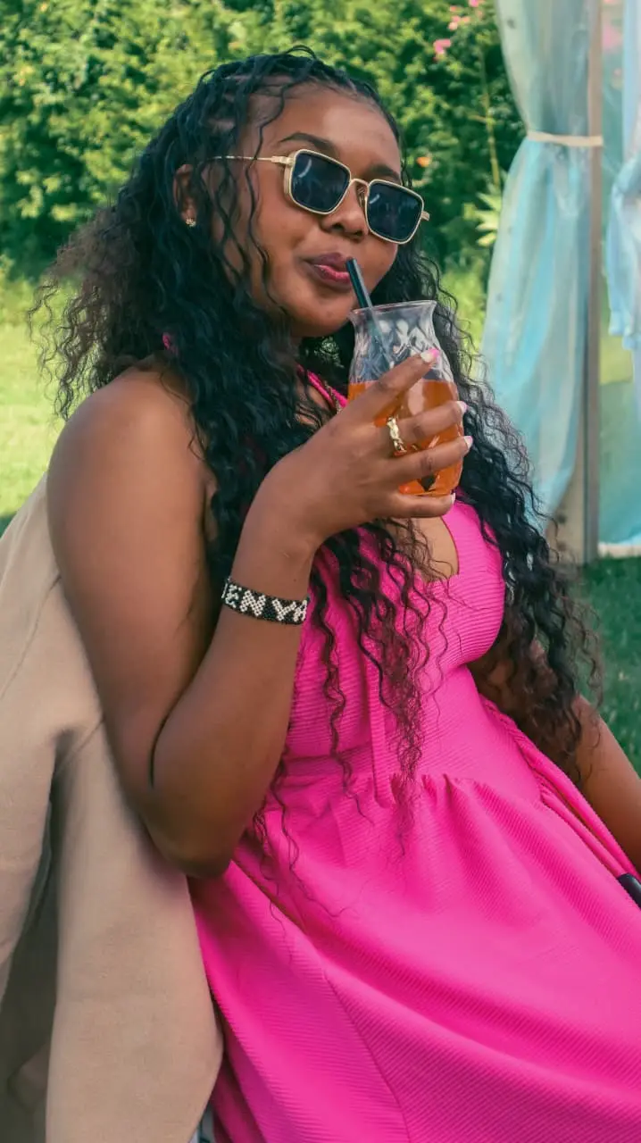 A woman in sunglasses sipping a drink under a garden marquee, entirely at ease